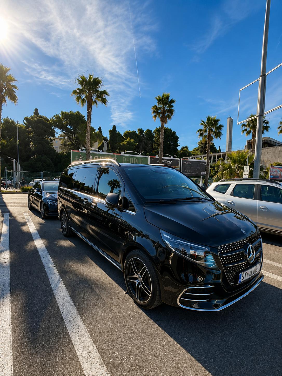 Black Mercedes-Benz V-Class and E-Class luxury transfer cars parked among palm trees in Split on a sunny day